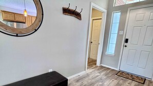 A hallway with a wooden bench, a round mirror, a wooden sign, and a door. - Covered JM Ranch - 3BR/2BA - Family Friendly (Lubbock)