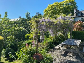 A garden with a wooden pergola covered in purple flowers, a gravel path, and a wooden bench. - Magnolia View (Barnstaple)