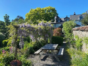 A garden with a wooden picnic table surrounded by lush greenery and flowering plants. - Magnolia View (Barnstaple)