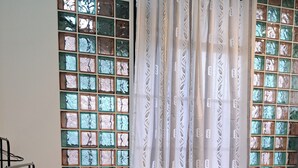 Ein Bett mit einem gemusterten Überwurf, zwei Kissen und ein Fenster mit dekorativer Verglasung und Vorhängen.