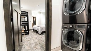 Ein Hotelzimmer mit einer Waschmaschine und einem Trockner, einem Bett, einer kleinen Sitzecke und einem Flur, der in ein weiteres Zimmer führt.