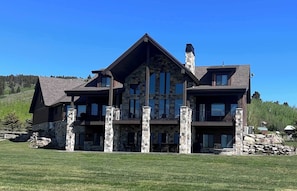 A large, multi-story house with stone and wood exterior, multiple windows, and a well-maintained lawn.