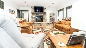 Ein Wohnzimmer mit Kamin aus Stein, Ledersofas, einem gemusterten Teppich und einem flachen Fernseher, der über dem Kamin angebracht ist.
