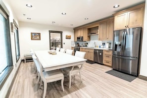 A modern kitchen with wooden cabinets, a stainless steel refrigerator, and a white dining table with chairs.