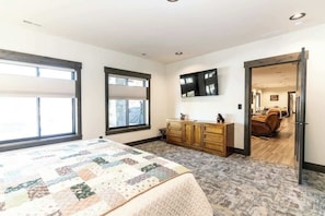 A bedroom with a large bed, a wooden dresser, and a view into another room.