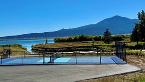 Ein Tennisplatz mit Netz, umzäunt und mit Blick auf einen See und Berge.