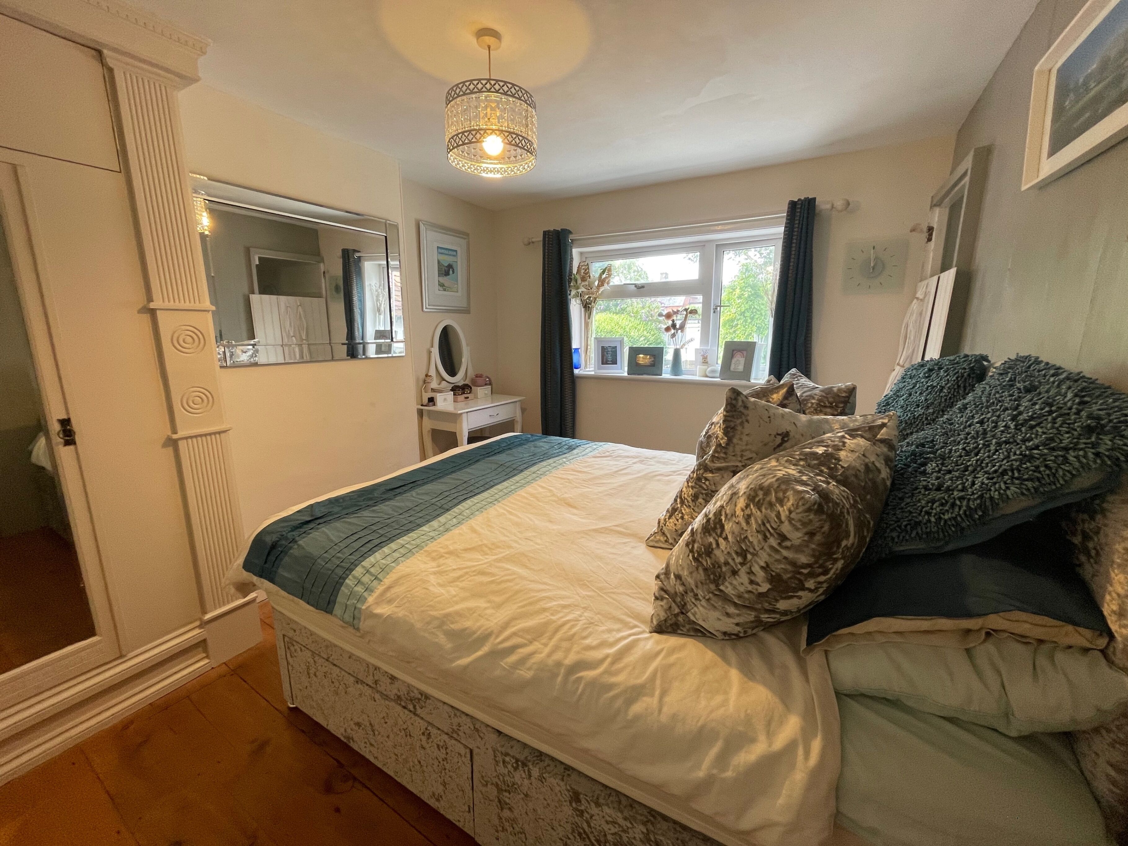 A bedroom with a bed, a dresser, a mirror, a window with curtains, and a chandelier.