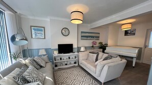 A living room with a sofa, a television, a piano, and a patterned rug. - Housesleeps7-parking-garden-fireplace-beachnearby (Wareham)