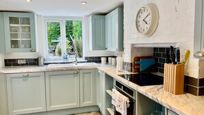 A modern kitchen with light blue cabinets, a marble countertop, a built-in oven, and a window with a view of greenery. - Housesleeps7-parking-garden-fireplace-beachnearby (Wareham)