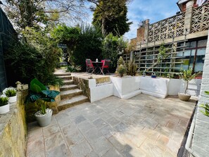 A courtyard with stone flooring, a seating area with chairs, and various potted plants. - Housesleeps7-parking-garden-fireplace-beachnearby (Wareham)