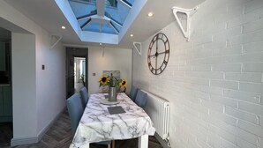 A dining area with a marble table, blue chairs, a vase with sunflowers, and a large clock on the wall. - Housesleeps7-parking-garden-fireplace-beachnearby (Wareham)
