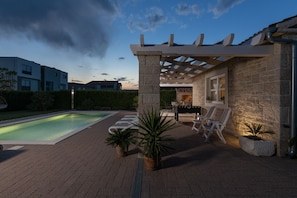 Une terrasse au bord de la piscine, agrémentée d’une pergola, de sièges et d’un mur en pierre.