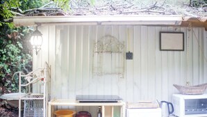 A rustic outdoor kitchen area with a metal grill, a laptop on a shelf, and various kitchen utensils.