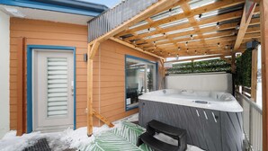 A wooden deck with a hot tub, a door, and a window.