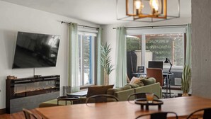 A modern living room with a flat-screen TV, a dining table, and a sofa.