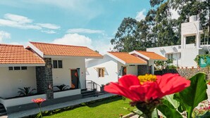 Una serie di edifici bianchi con tetti in tegole arancioni, un muro in pietra e una piccola area giardino con fiori.
