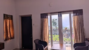 Una stanza con una porta, due sedie, un tavolo e vista su un balcone con ringhiera e piante.