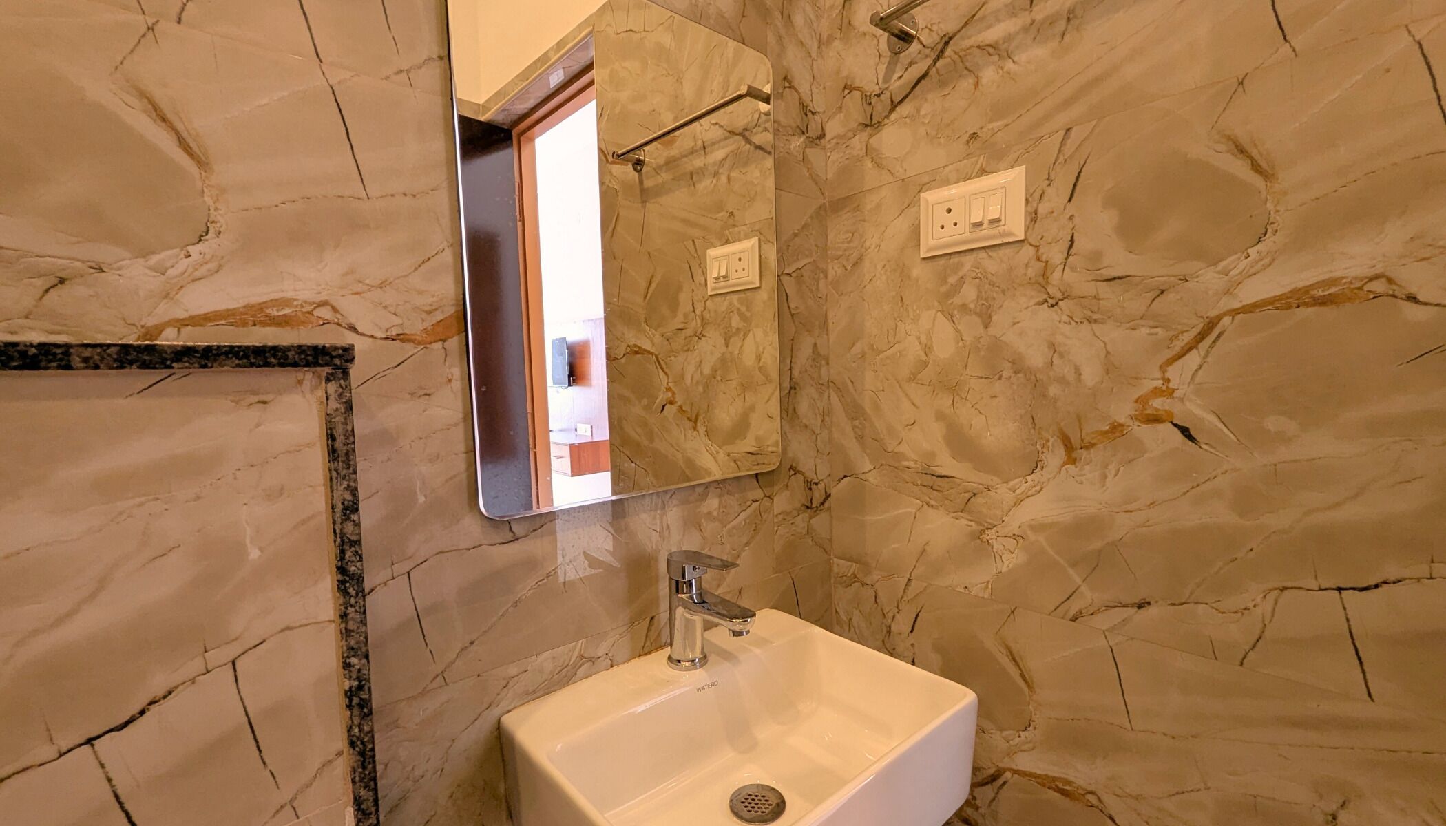 Une salle de bain avec un mur en marbre, un lavabo et un miroir.