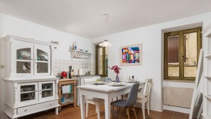 A kitchen with a white cabinet, a dining table with chairs, a calendar, and a window with a view. - Apartment Dei Fiori 1 (Rovinj)
