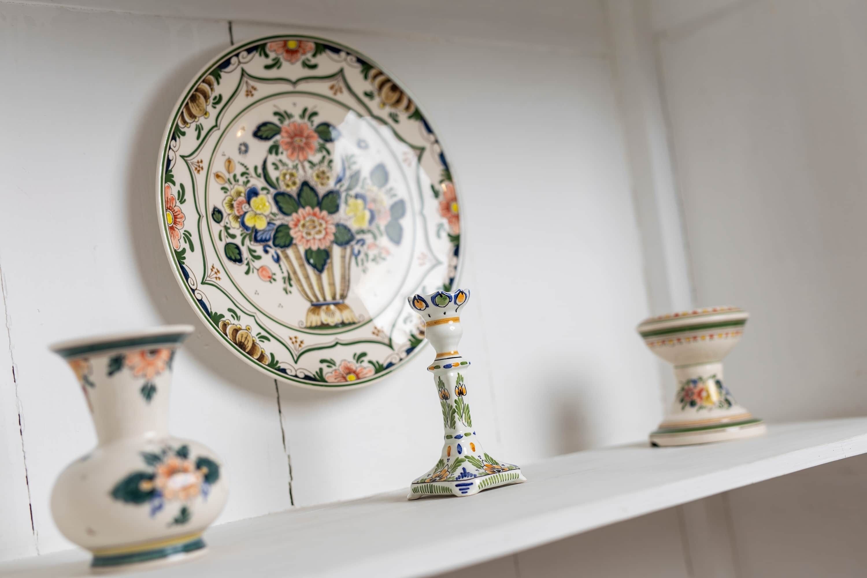 Une étagère blanche ornée d’une assiette décorative, d’un vase et d’un chandelier.