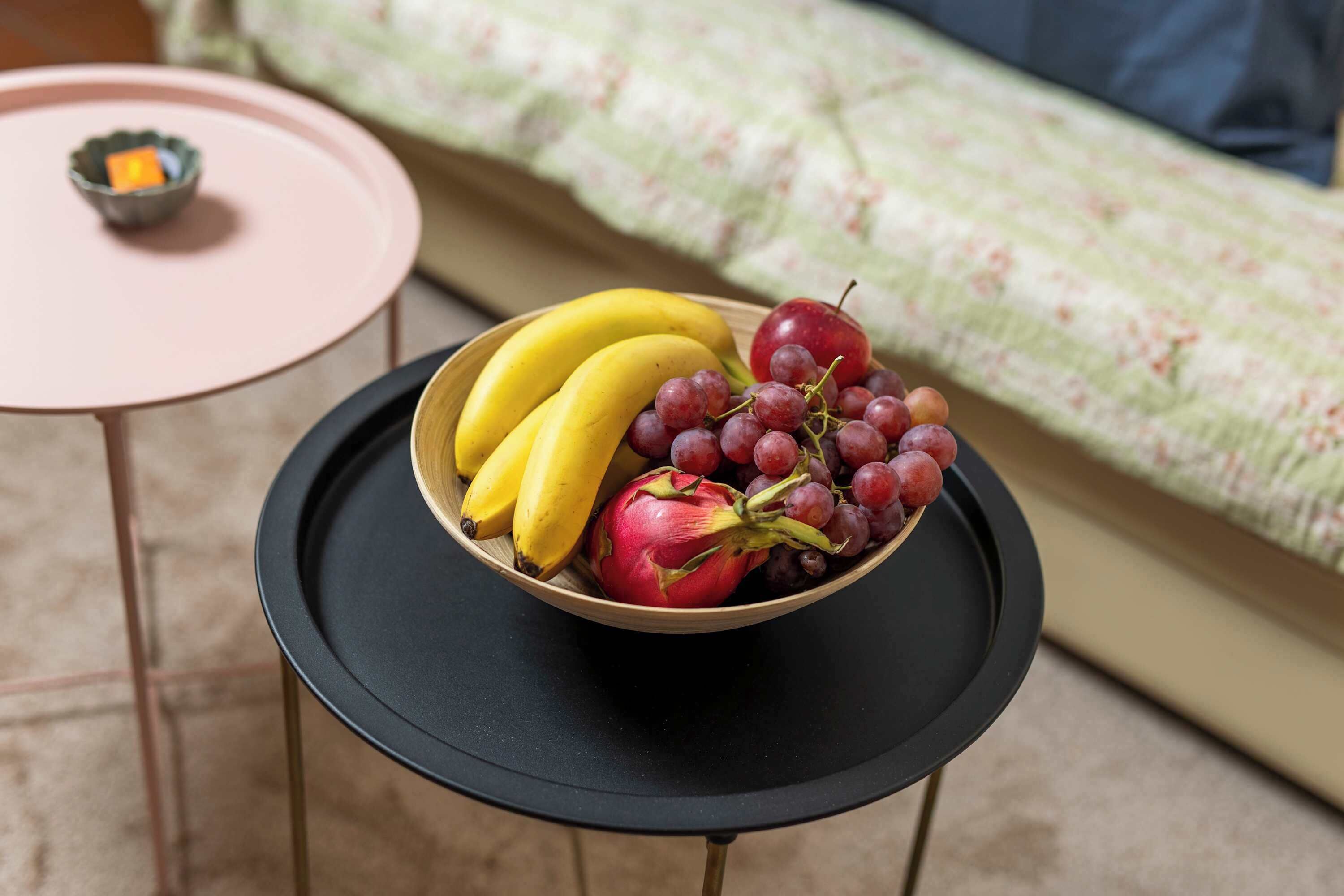 Un frutero con fruta sobre una mesita, con un cojín de fondo.
