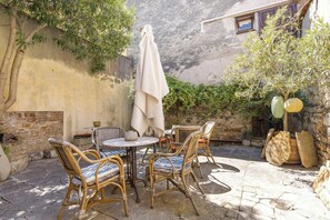 Een terras van natuursteen met rieten meubels, een tafel en een overdekte parasol.