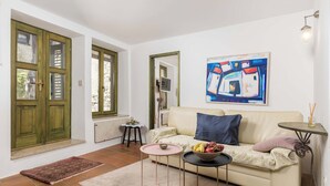 A room with a sofa, a small table with a bowl of fruit, a rug, and a painting on the wall. - Apartment Dei Fiori 1 (Rovinj)