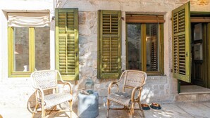 A stone building with green shutters, wicker chairs, a small table, and pet bowls outside. - Apartment Dei Fiori 1 (Rovinj)