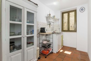 Eine Küche mit weißen Schränken, einer kleinen Arbeitsplatte und einem Fenster mit grünem Rahmen.