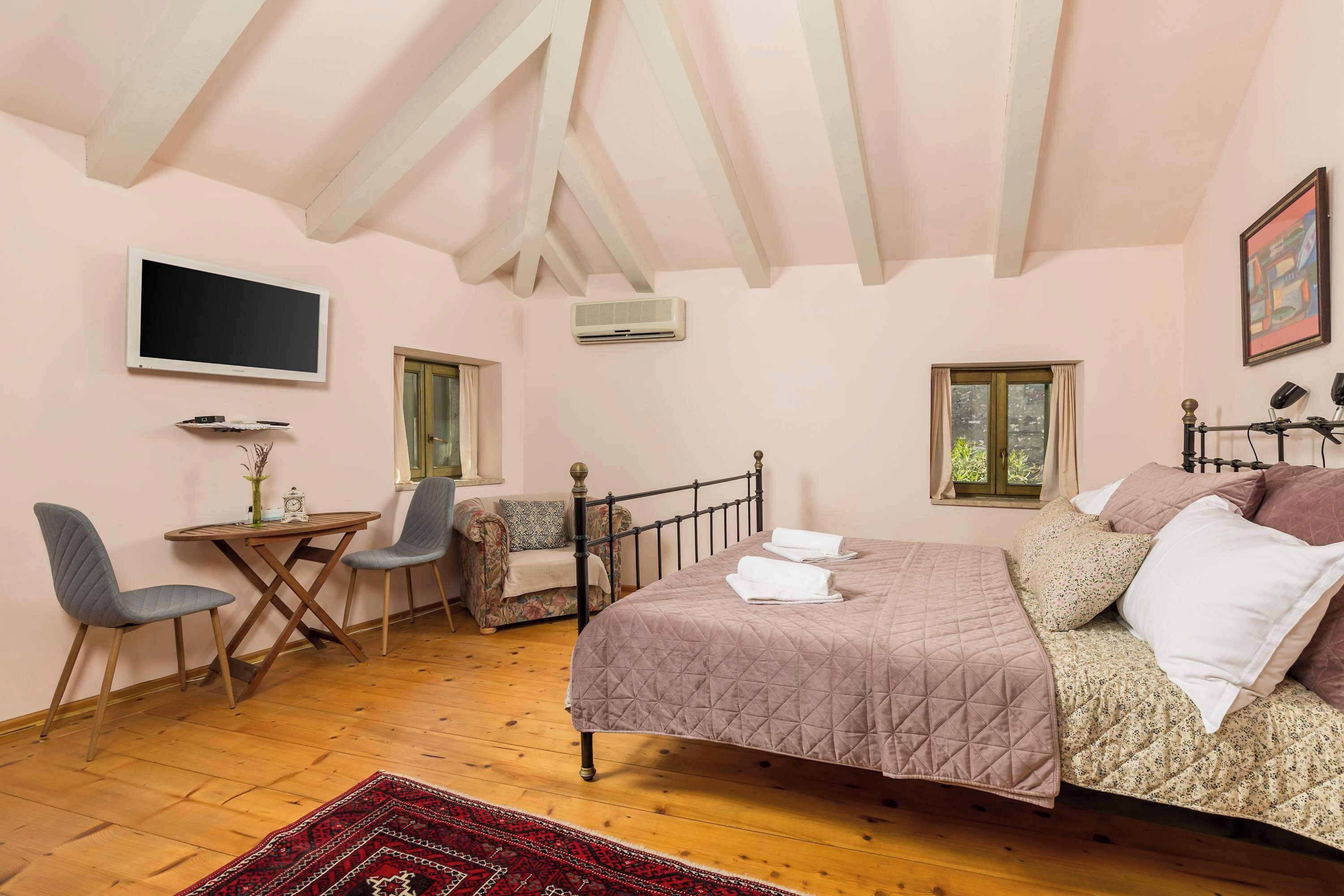 Ein Schlafzimmer mit Bett, Schreibtisch, zwei Stühlen, einem Fernseher und einem Fenster.