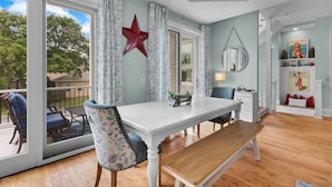 A dining area with a white table, blue patterned chairs, and a red star decoration on the wall. - Rooftop Deck, Soaring Views & Steps to Tybee’s Best Beaches by Tybee Cottages (Tybee Island)