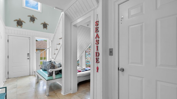 A spacious hallway with a staircase leading to a bedroom. A bench with pillows is placed near the entrance. - Rooftop Deck, Soaring Views & Steps to Tybee’s Best Beaches by Tybee Cottages (Tybee Island)