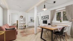 A modern living room with a sofa, dining table, and chairs. There is a bookshelf, a TV, and a window with curtains. - Secret Steps Apartment (Rovinj)