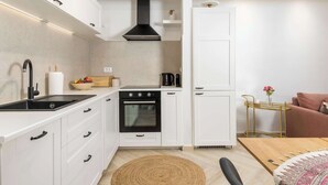 A compact kitchen with white cabinets, a black stove, and a small refrigerator. - Secret Steps Apartment (Rovinj)