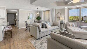 A spacious living area with a sofa, ottoman, and glass coffee table. There is a dining area with a table and chairs, and a ceiling fan. - Brighton 107 3 Br in Kingston Beach, Pool (Myrtle Beach)