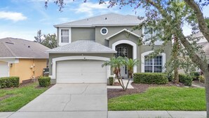 A two-story house with a garage, a front yard with a palm tree, and a neighboring house. - PROMO Villains Lair 8 BR Home, Private Pool - by Blue Sky Villas (Kissimmee)