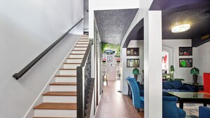 A staircase with wooden steps and a black handrail leading to a living area with blue sofas and a red chair. - PROMO Villains Lair 8 BR Home, Private Pool - by Blue Sky Villas (Kissimmee)