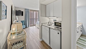 Eine moderne Küche mit Mikrowelle, Spüle und Schränken, ein Essbereich mit Glastisch und Stühlen sowie ein Balkon mit Blick auf hohe Gebäude.