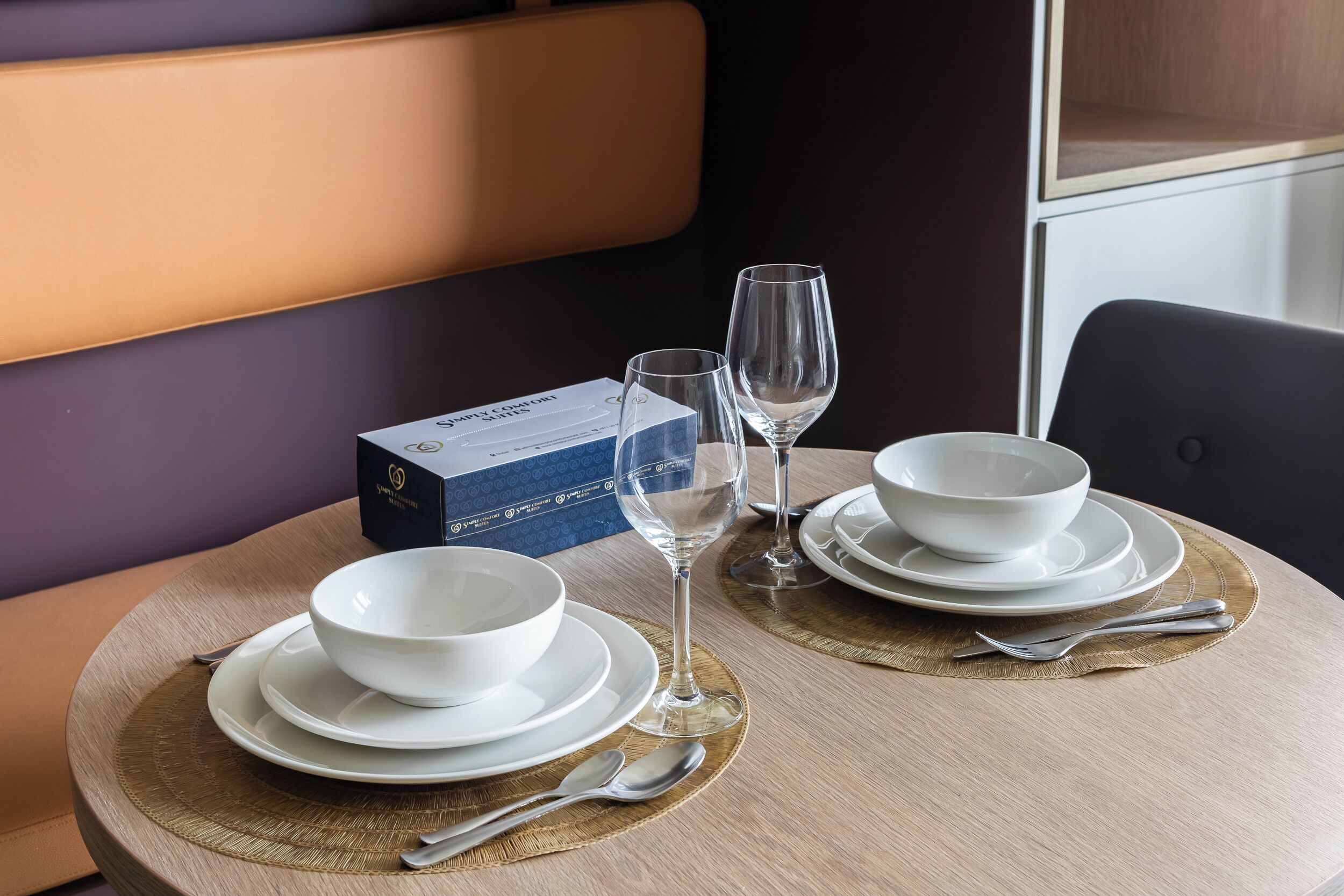 A dining table with white bowls, wine glasses, and a box of champagne.