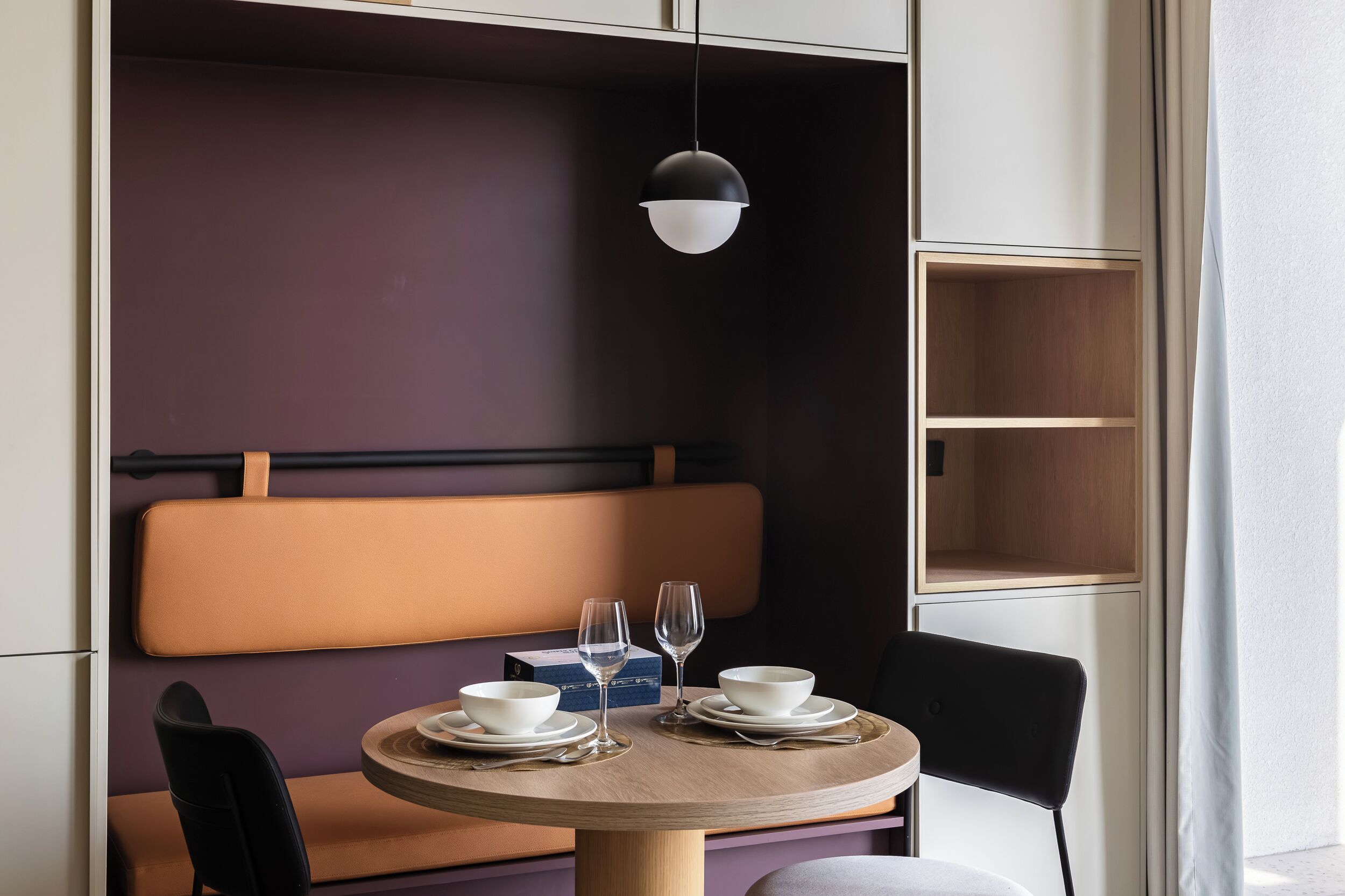 A dining area with a round table, two chairs, a bench, and a pendant light.