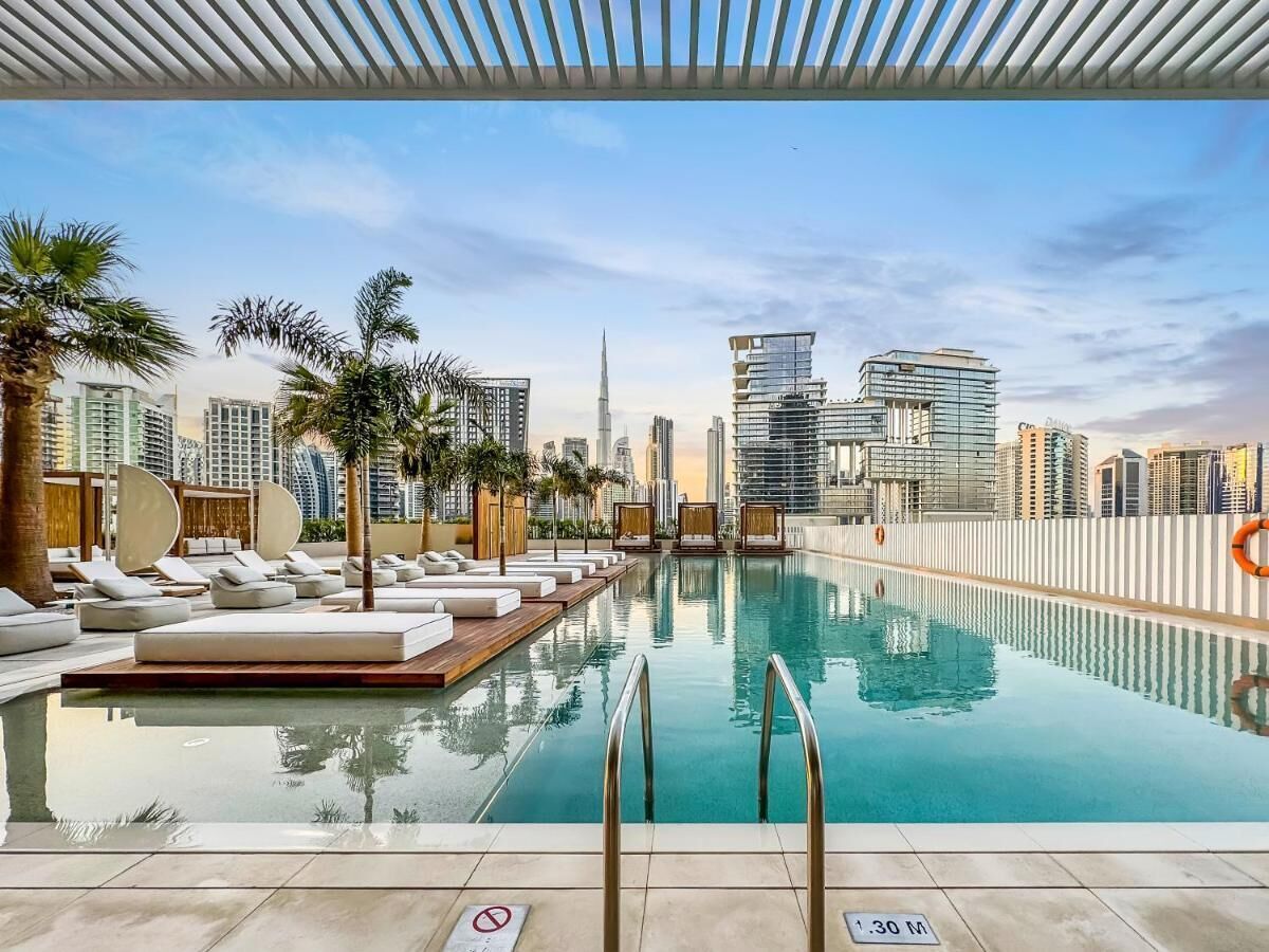 Une piscine sur le toit, avec des chaises longues, des palmiers et une vue sur les toits de la ville en arrière-plan.