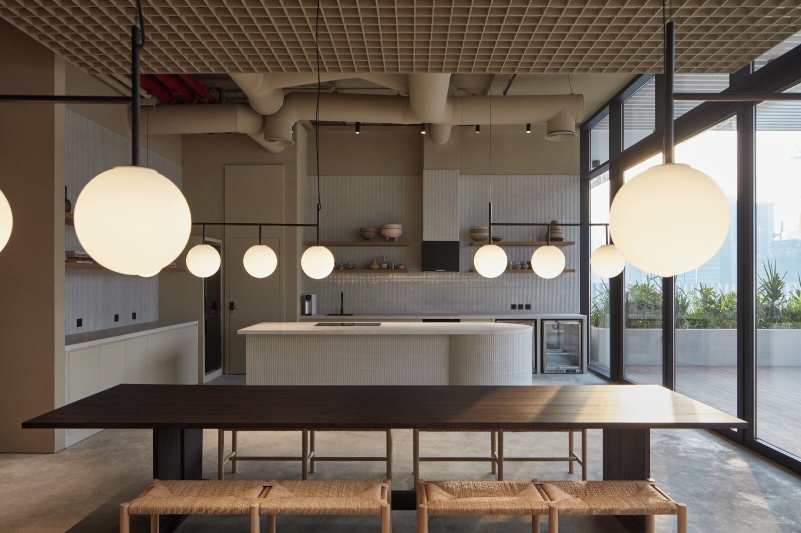 Une cuisine moderne dotée d’un grand îlot central, de luminaires suspendus et offrant une vue sur la ville.