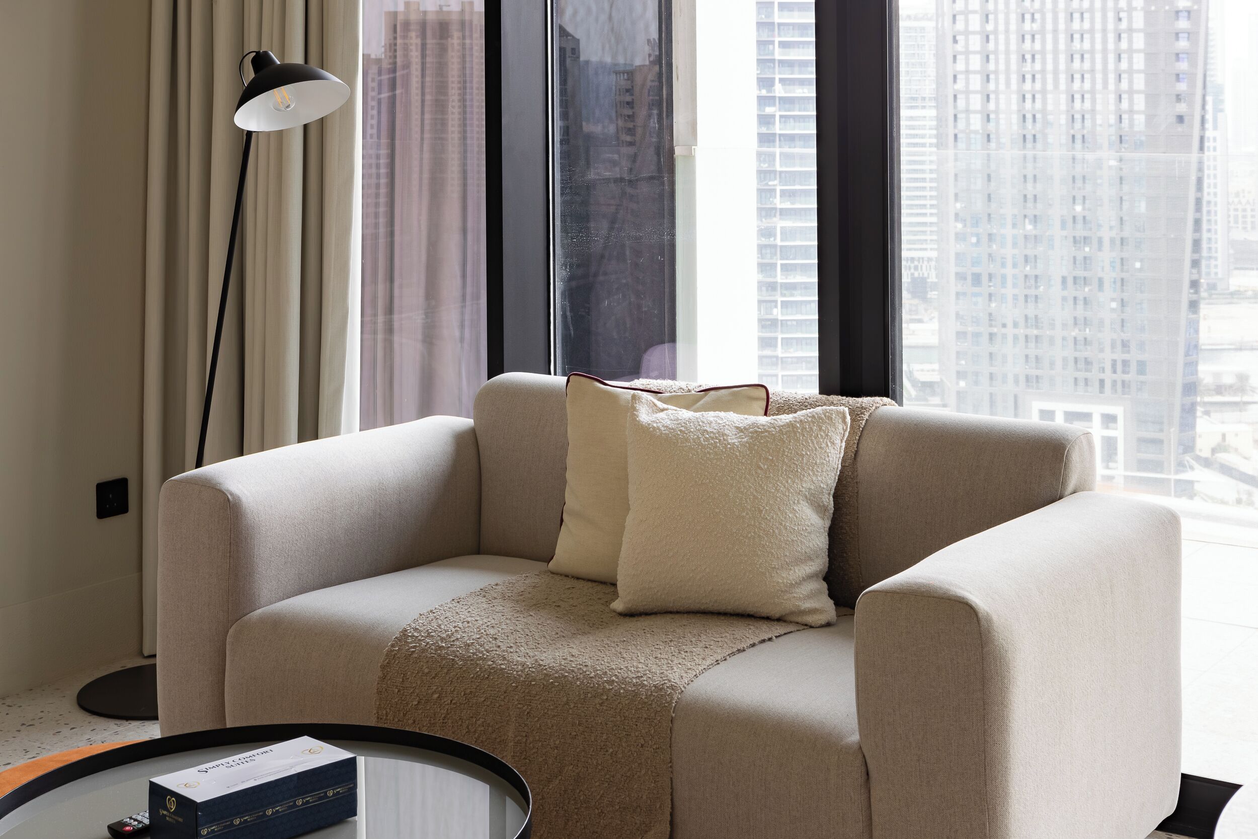 Un salon moderne avec un canapé beige, un plaid et une télécommande posée sur une table d’appoint.