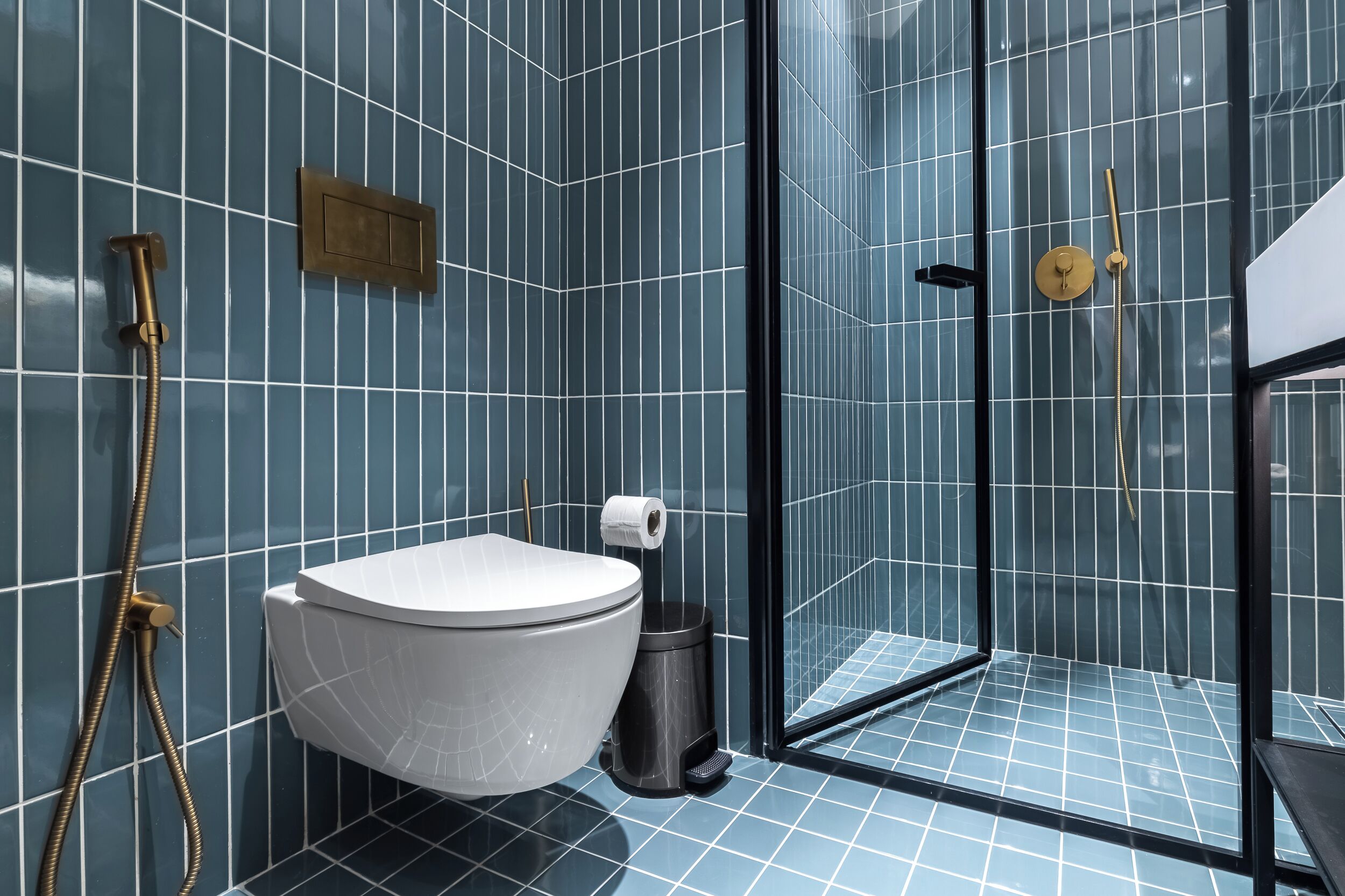 Une salle de bain moderne comprenant des toilettes, une poubelle et une douche séparée par une paroi en verre.