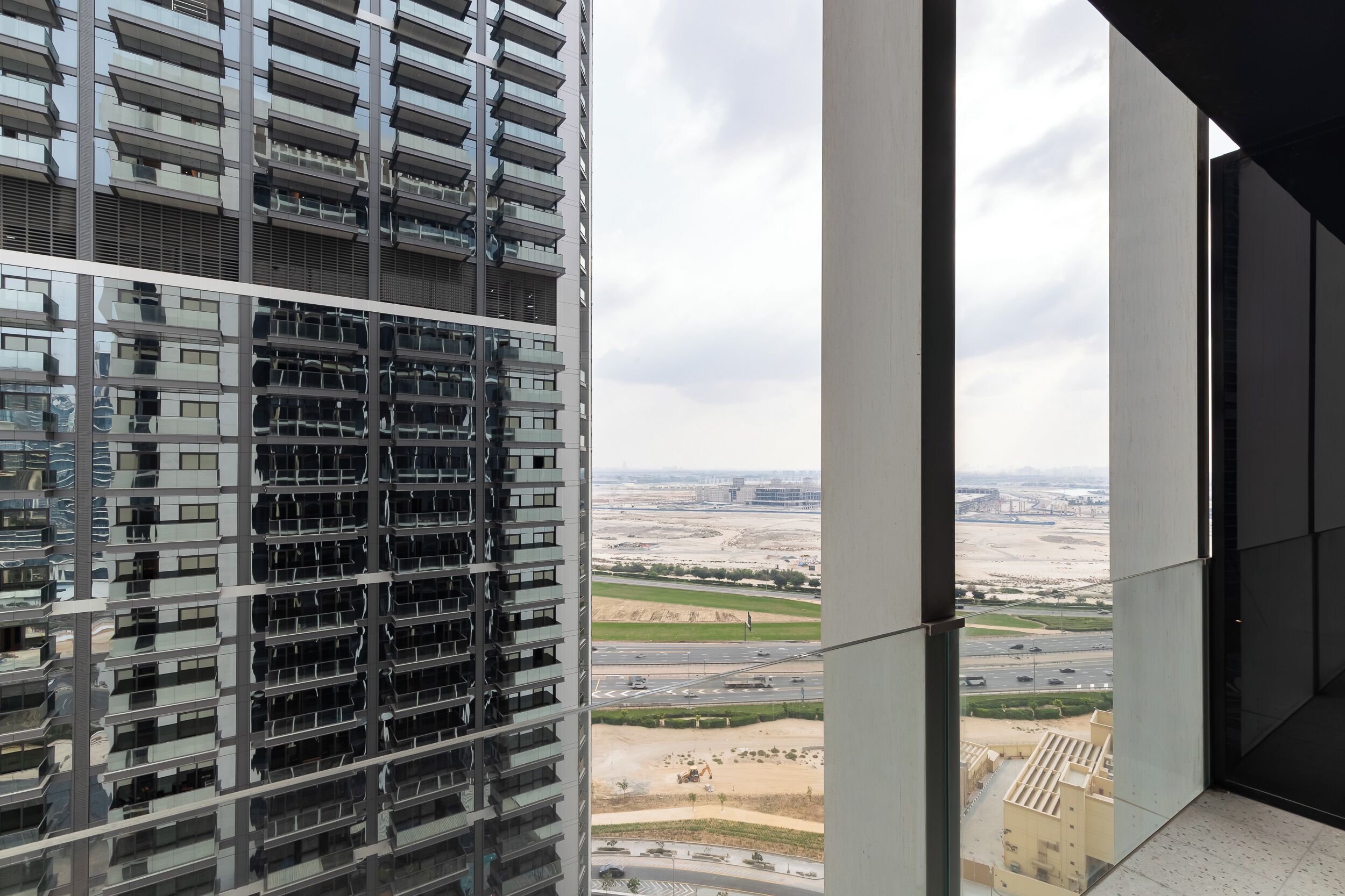 A high-rise building with multiple balconies and a view of a construction site and roads.