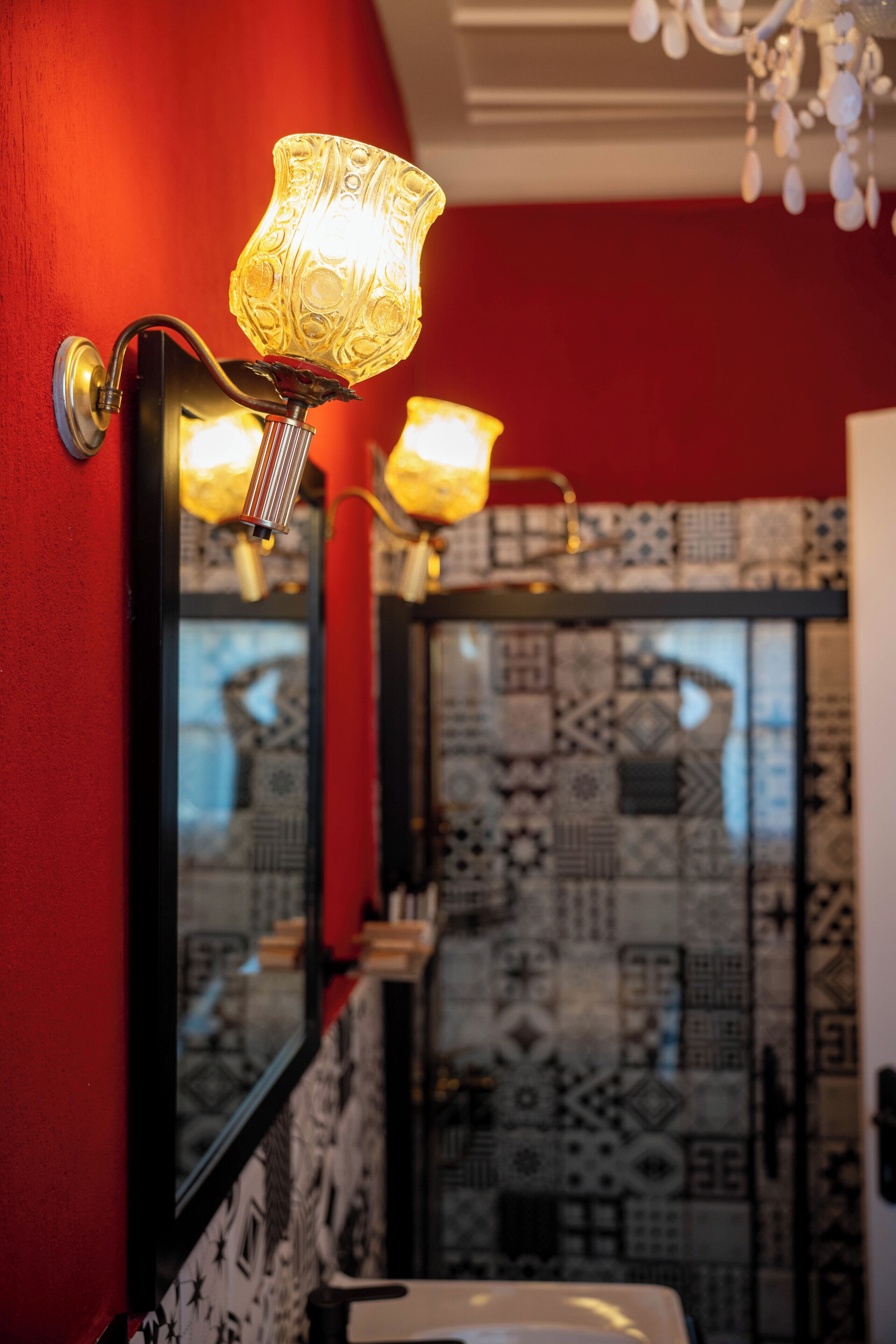 Une salle de bain avec des carreaux décorés, un mur rouge et un miroir agrémenté d’un luminaire.