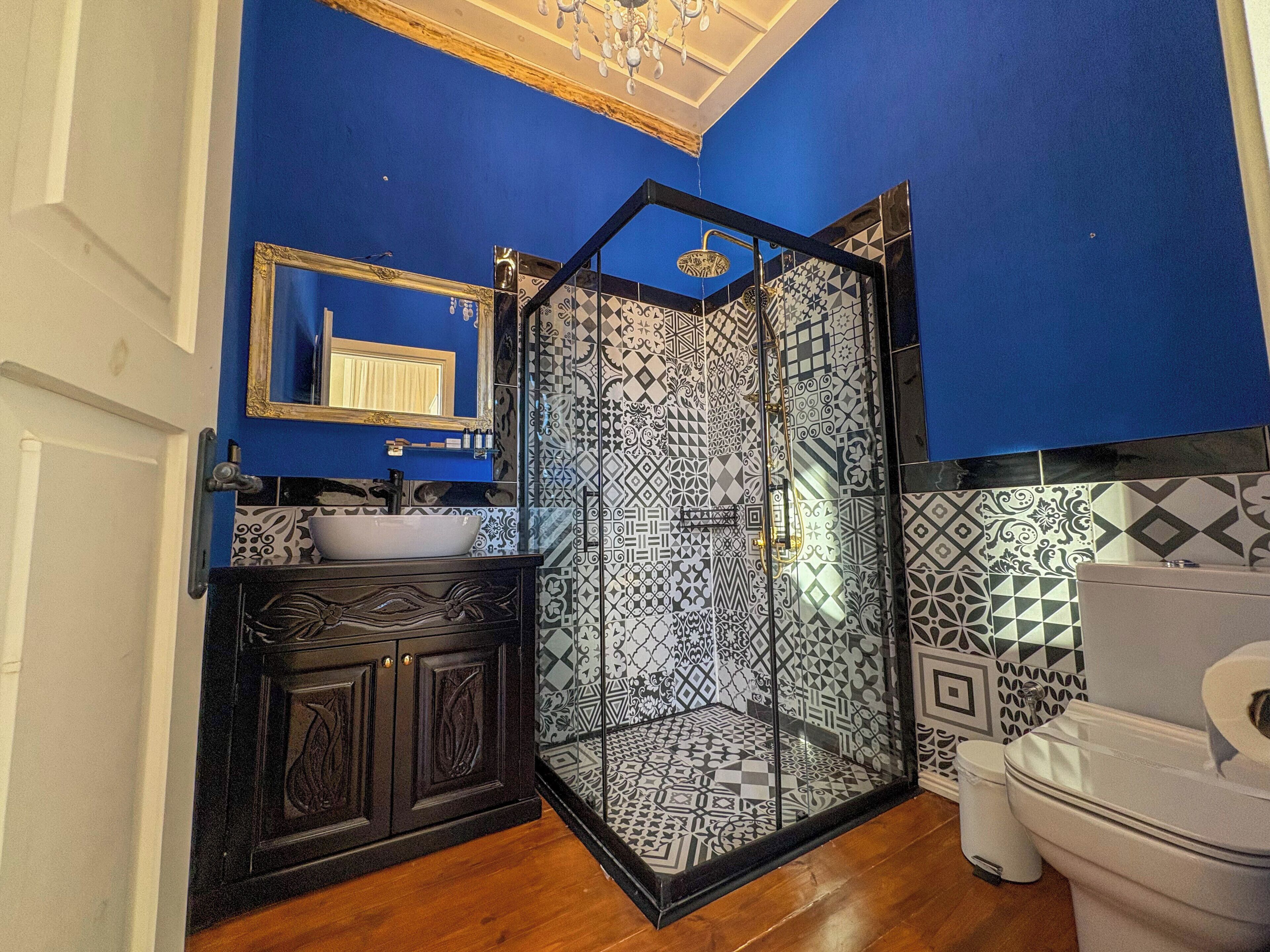 A bathroom with a blue wall, a white sink, a black cabinet, a glass-enclosed shower, and a white toilet.