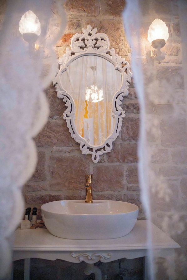 Un baño con un lavamanos blanco, un espejo decorativo y dos luces empotradas.