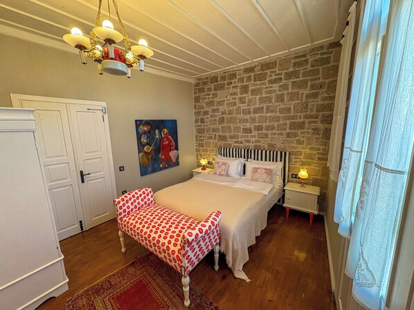 Un dormitorio con cama, un banco, una araña, un cuadro y una pared de piedra.