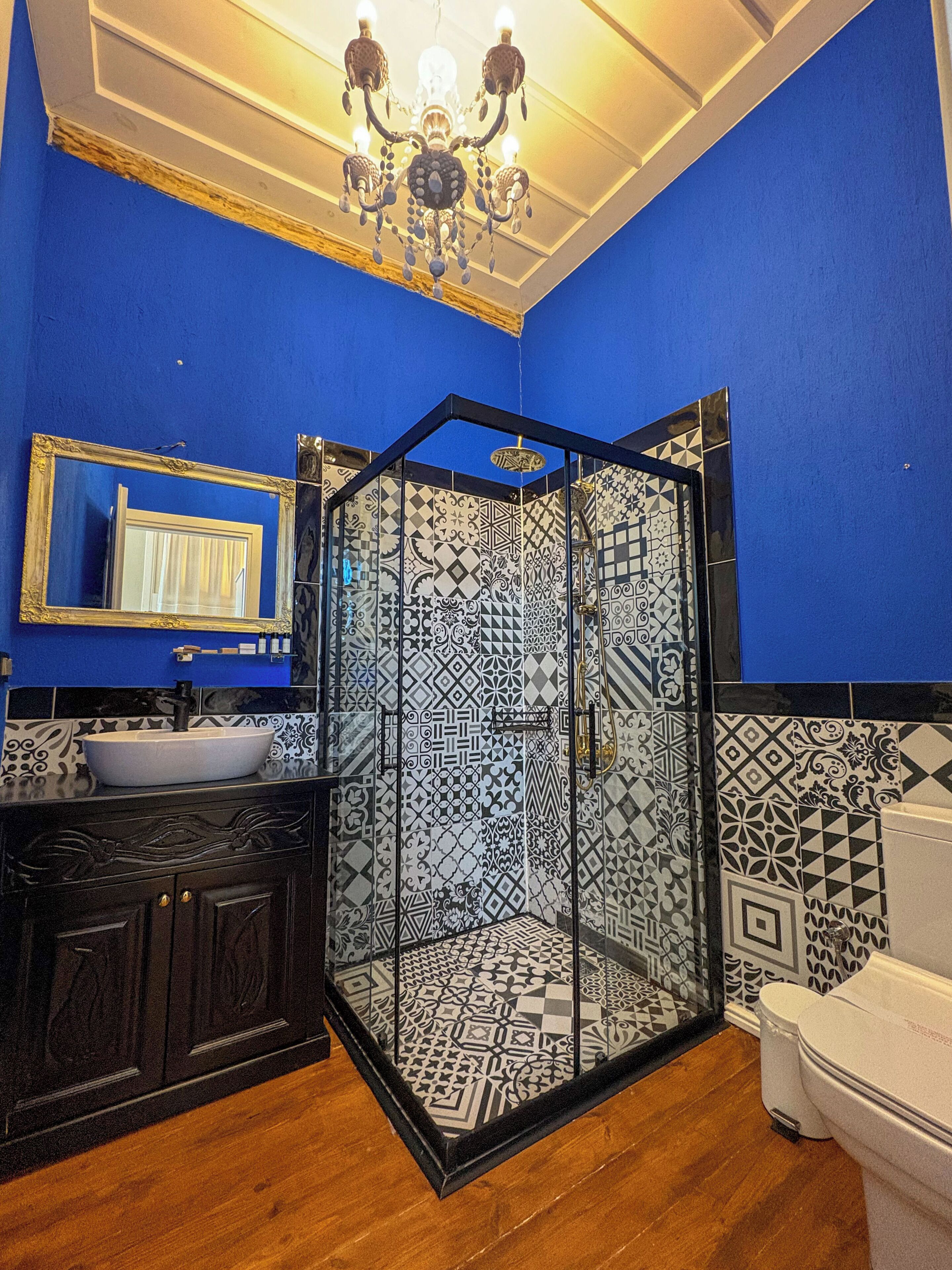 A bathroom with a blue wall, a black and white patterned shower enclosure, a white sink, and a mirror with a gold frame.